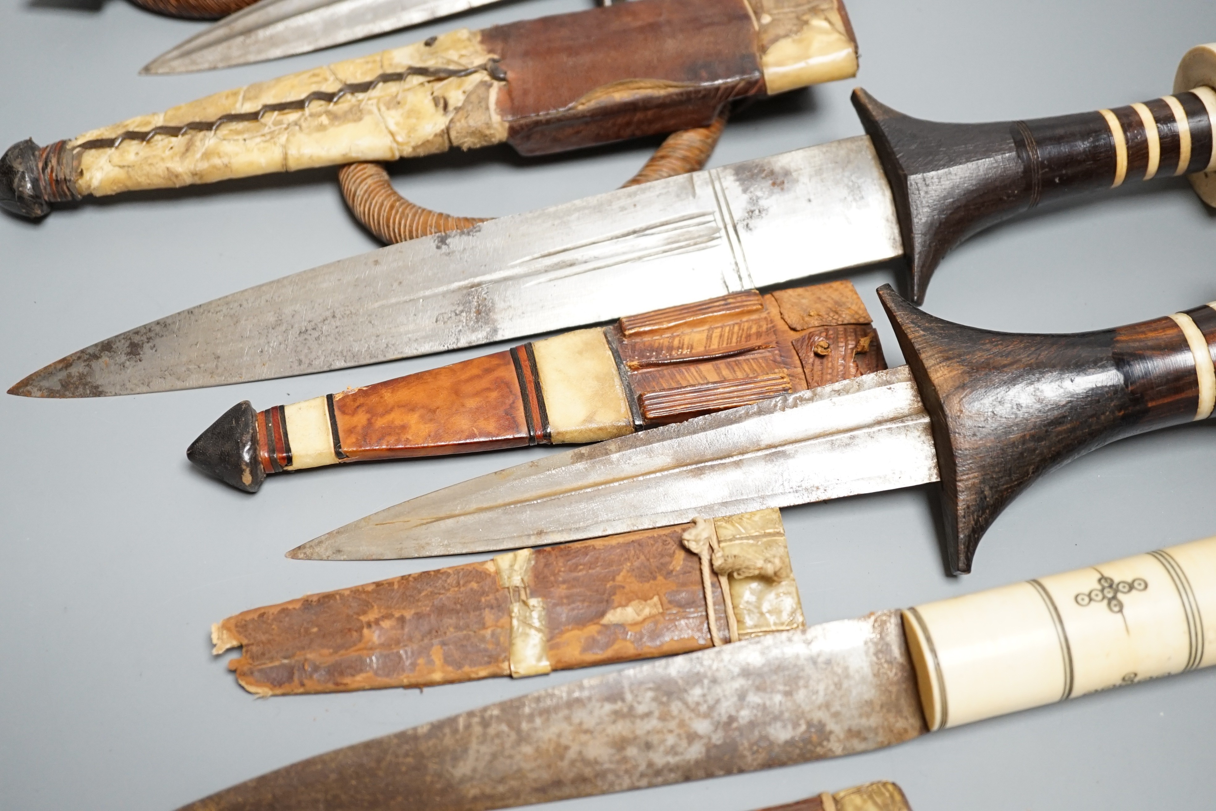 Five assorted African Nilotic tribal daggers c.1900, comprising three with turned ivory mounted ebony handles (two with silver pommels); and two further with cylindrical ivory handles, all in their leather sheaths, maxim